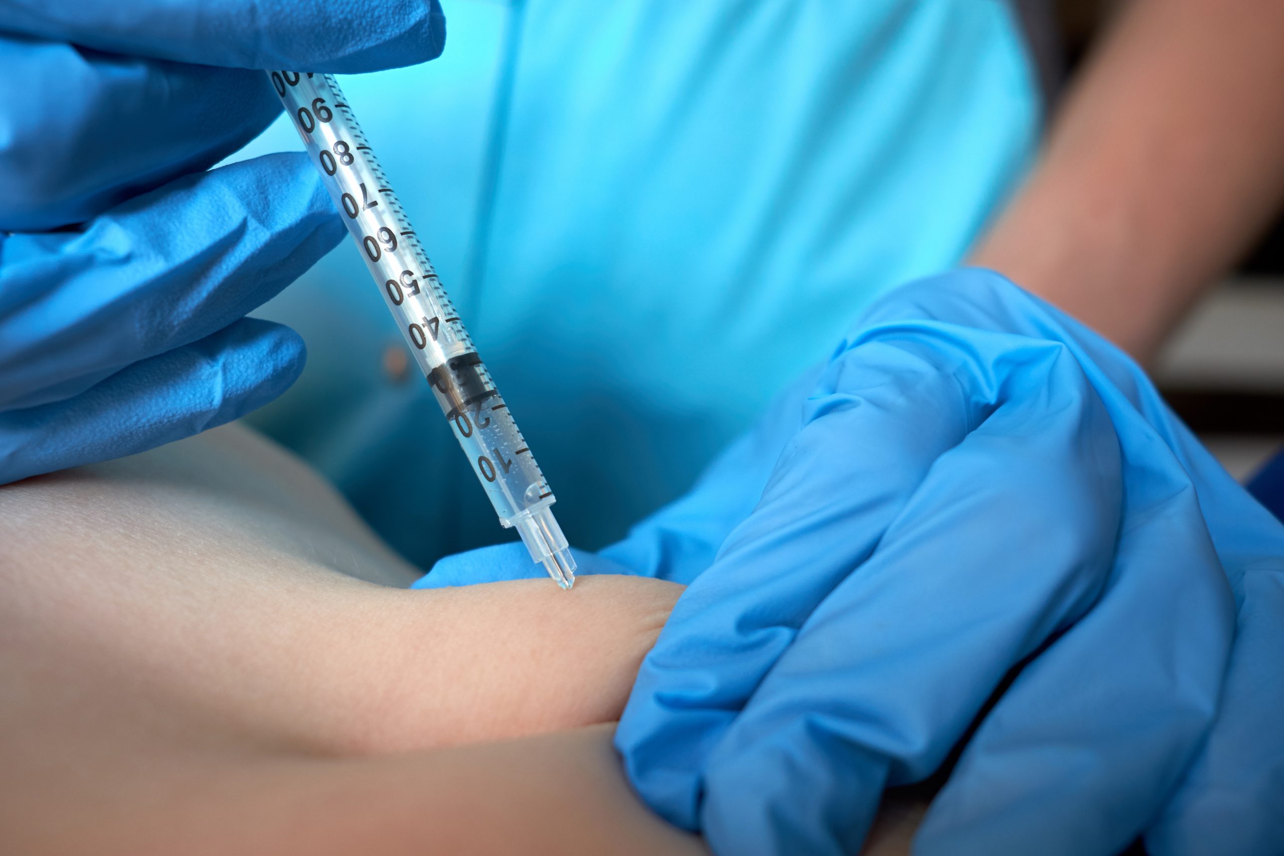 Hands of nurse in blue surgical gloves making injection of anticoagulant subcutaneously to child. Closeup view.