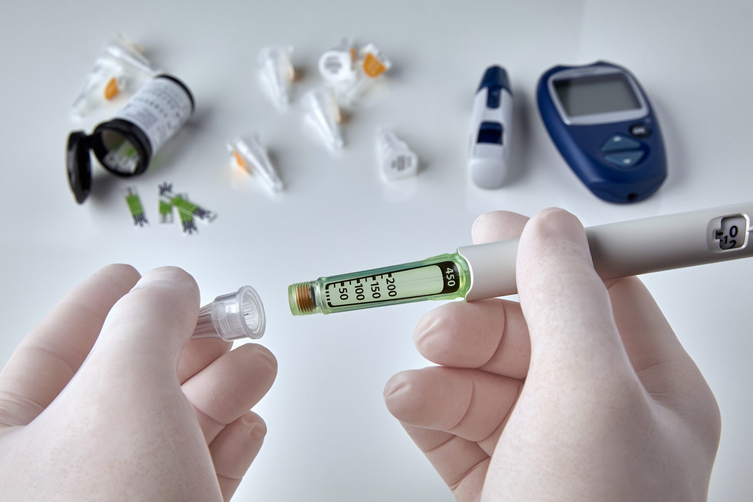 Hands in silicone gloves with a syringe against the background of a glucometer and test strips. Installing the needle on the syringe pen